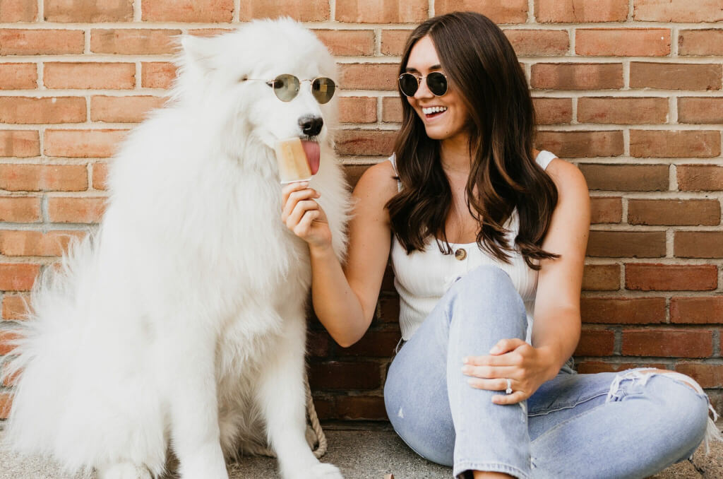 large white dog enjoying bone broth pup-sicle with woman